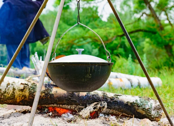 A camp-steaky sooty food bowl hanging on a tripod over a fire — Stock Photo, Image