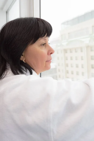 Middelbare leeftijd vrouw door het raam — Stockfoto