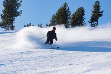 Bulgaristan. Bansko. 10 Şubat 2020. Büyük kar tarlasında kayak yapan kayakçı. Kar tozu sıçratıyor.