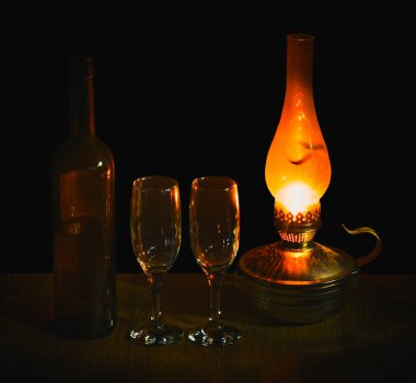 Gazyağı lambasının loş ışığında bir şişe kırmızı şarap ve iki bardak siyah üzümün arka planına karşı.