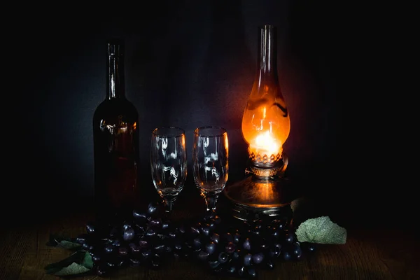 在煤油灯昏暗的灯光下 一瓶红酒和两杯黑葡萄背景的酒杯 — 图库照片