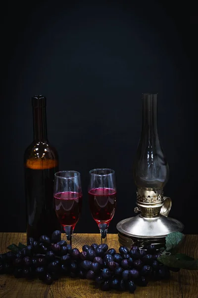 在煤油灯昏暗的灯光下 一瓶红酒和两杯黑葡萄背景的酒杯 — 图库照片
