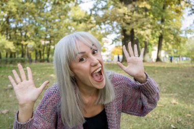 Açık havada komik suratlar yapan bir kadının portresi. Gümüş saç..