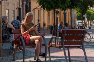 TIMISOARA, ROMANIA - 16 Eylül 2016: Bir bankta oturan ve telefonunu kontrol eden kadın. Gerçek insanlar..
