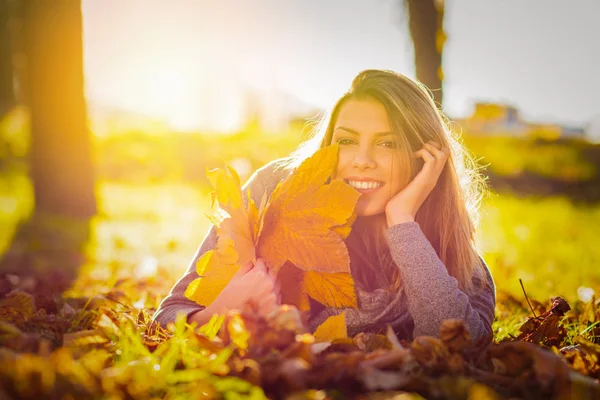 Šťastná mladá žena v parku na podzim drží listy a relaxaci — Stock fotografie