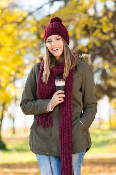 Happy young woman in autumn in park with takeaway coffee — Stock Photo, Image