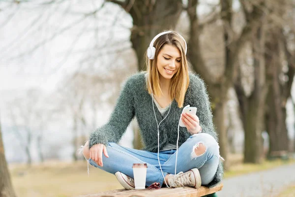 Chica adolescente en el parque en otoño con teléfono inteligente y auriculares —  Fotos de Stock