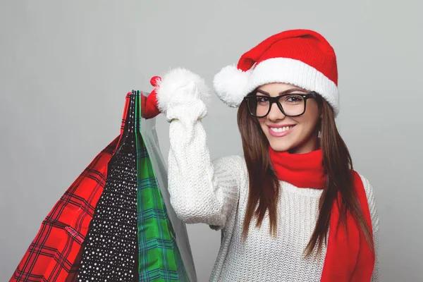 Jonge vrouwelijke shopper in Kerstman hoed en bril holding boodschappentassen glimlachen — Stockfoto