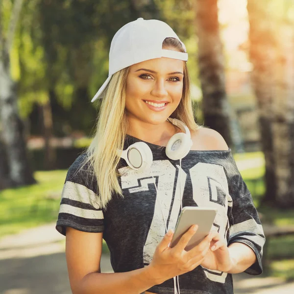 Fresco ragazza adolescente millenaria con smart phone e cuffie sorridenti all'aperto nel parco — Foto Stock