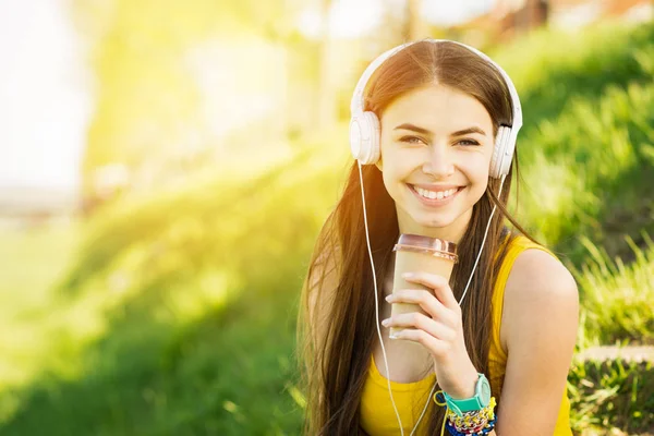 Adolescente con auriculares bebiendo café para llevar al aire libre en el parque en verano —  Fotos de Stock