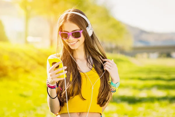 Chica adolescente en el parque en verano con teléfono inteligente y auriculares —  Fotos de Stock