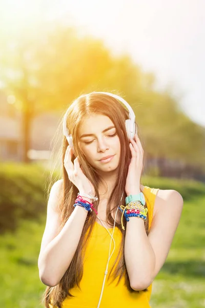 Millennial teenage girl listening to music on headphones in park in summer — Stock Photo, Image