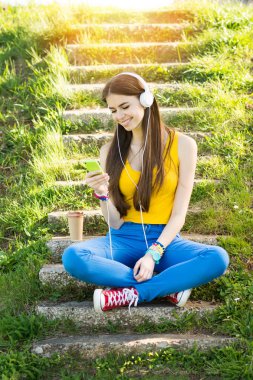 Yaz kulaklıklarla, parkta genç kadın akıllı telefon ve paket servisi olan restoran kahve