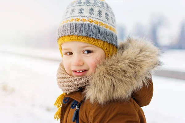 雪の冬の日に屋外で幸せな幼児の男の子のクローズアップポートレートファジィ毛皮の帽子のジャケットと編んだビーニーを着て — ストック写真