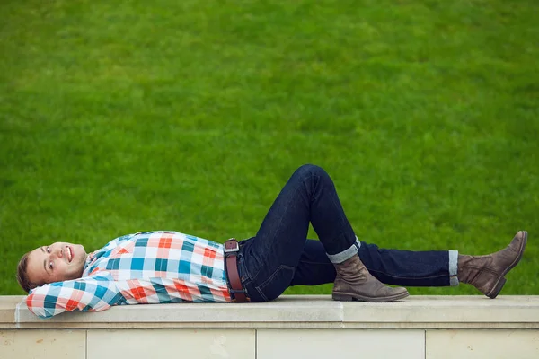 Retrato de feliz joven feliz hombre relajante cerca de césped verde en el parque —  Fotos de Stock