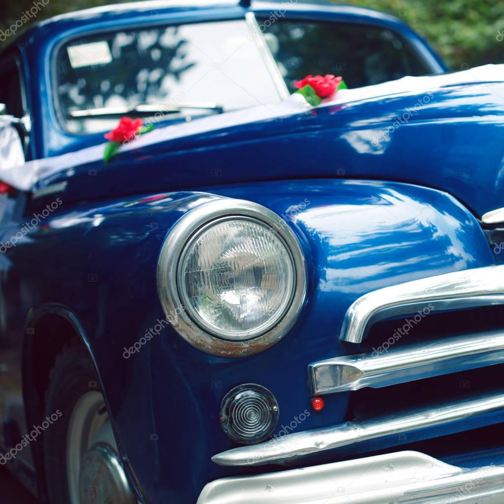 Blue colored vintage wedding car decorated with roses and white ribbon