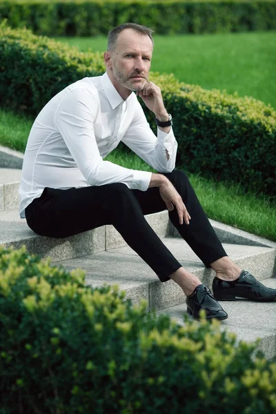 Luxurious and stylish concept. Rich mature man sitting on marble stairs — Stock Photo, Image