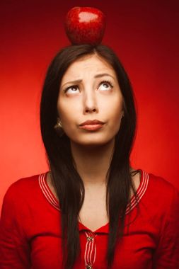 Başında Kırmızı elma ile kırmızı arka plan üzerinde poz güzel öğrenci kız portresi. Eğitim kavramı. Mükemmel uzun saç, doğal makyaj. Hippi tarzı. Yakın çekim. Stüdyo vurdu