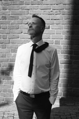 Smart casual yakışıklı olgun adam Avrupa şehri bina ve kameraya bakarak eski ev üzerinde duruyor. Elleri ceplerinde. Grafik gölgeler. Tek renkli açık vurdu