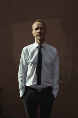 Smart casual yakışıklı olgun adam Avrupa şehri bina ve kameraya bakarak eski ev üzerinde duruyor. Elleri ceplerinde. Derin gölgeler. Açık atış