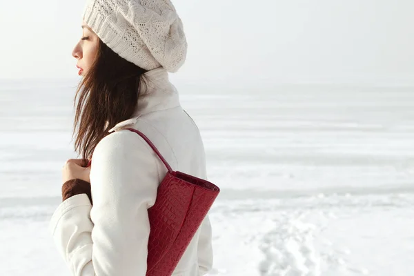 情绪化的配置文件中白色外套和贝雷帽离合器和摆在冬季海边举行红色皮革时尚模型的画像 阳光明媚的天气 法国风格 室外拍摄 — 图库照片