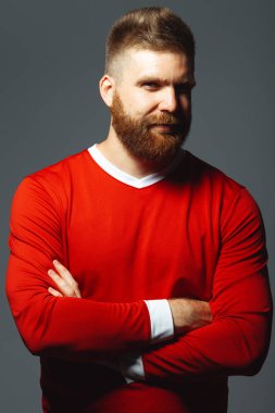 Portrait of smiling proud handsome middle aged red-haired sportsman over gray wall with crossed hands. Red sportswear. Football player. Lumberjack style. Vertical studio shot clipart