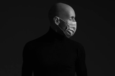 Coronavirus, Biyolojik Koruma Konsepti. Tıbbi maske takan yakışıklı kel bir adamın profil portresi, siyah balıkçı yaka kazak ve dua. Kopyalama uzayı. Stüdyo çekimi
