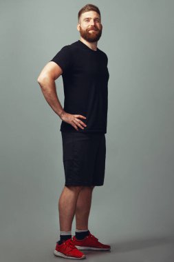 Spor kıyafetleri konsepti. Açık gri arka planda poz veren, 30 yaşında, tatlı, güler yüzlü, kaslı, kızıl saçlı bir adamın tam boy portresi. Mükemmel saç kesimi. Stüdyo çekimi