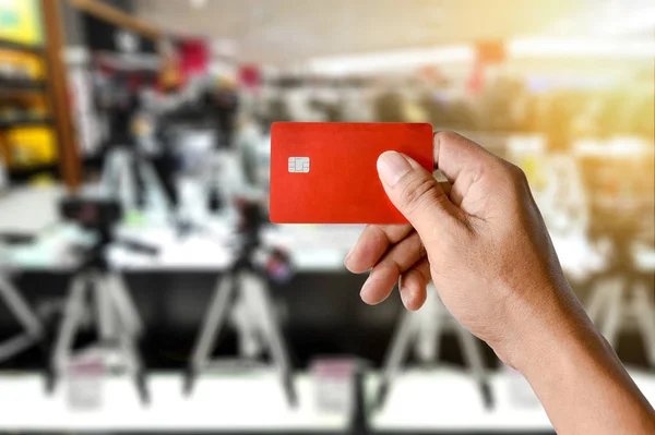 Uma mão segurando cartão de crédito na loja de câmera borrada — Fotografia de Stock