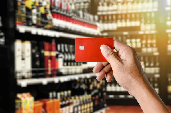 Um cartão de crédito mão segurando no fundo loja Wine Supermarket — Fotografia de Stock