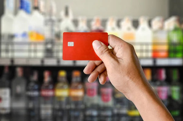 Um cartão de crédito mão segurando no fundo loja Wine Supermarket — Fotografia de Stock