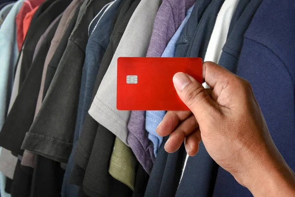 Uma mão segurando cartão de crédito em t-shirts rack na loja — Fotografia de Stock