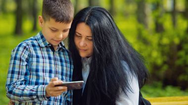 Küçük çocuk cep telefonu ve bir sarı bankta oturan annesi oynamaya.