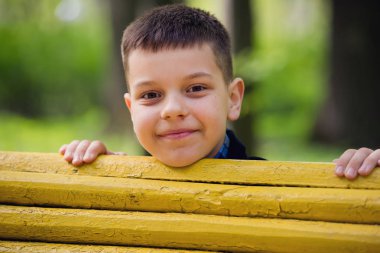 Küçük bir çocuk sarı bir Bank arkasından bakıyor.