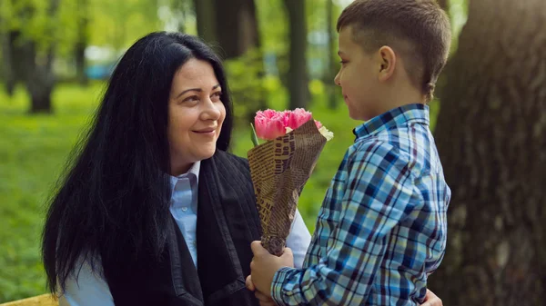 Сын подарил матери свежий букет цветов тюльпанов на скамейке в парке . — стоковое фото