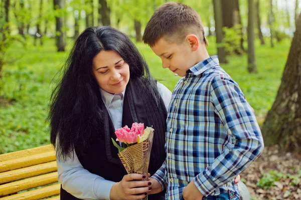 Сын подарил матери свежий букет цветов тюльпанов на скамейке в парке . — стоковое фото