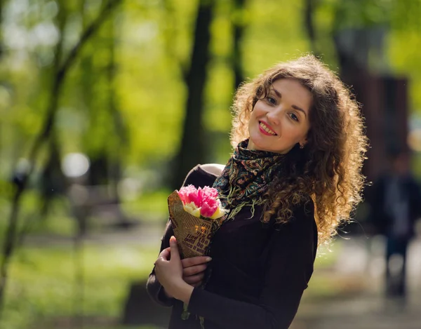 Mooie roodharige meisje in een park met een boeket van bloemen. — Stockfoto