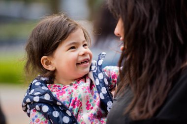 Annesinin kollarında küçük bir kızı ona bakar ve gülüyor. Anneler günü.