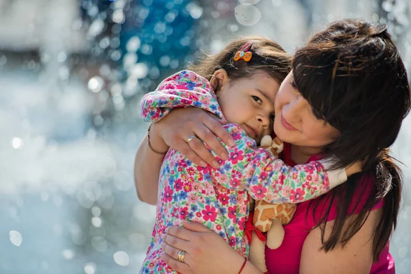 Маленькая очаровательная девочка обнимает свою мать в парке возле фонтана. День матери . — стоковое фото