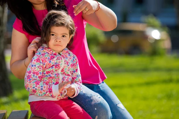 Мама робить зачіску з малою чарівною донькою в парку на лавці. День матері. Закри. — стокове фото