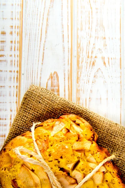 Fresh bakery. Top view of baked pie with apples on sackcloth on a white wooden background. Rustic style. — Stock Photo, Image