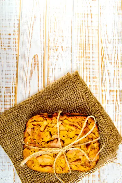 Taze ekmek. Beyaz ahşap zemin üzerinde çul üzerinde üstten görünüm pişmiş turta elmalı. Rustik tarzı.