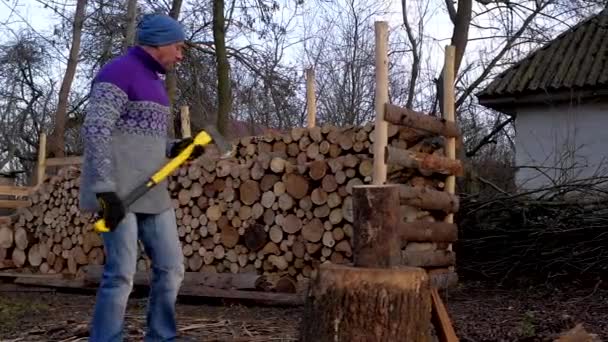 Muž, dřevorubec s žlutým ax naštípat dřevo na oheň na pozadí hromadu dříví. — Stock video