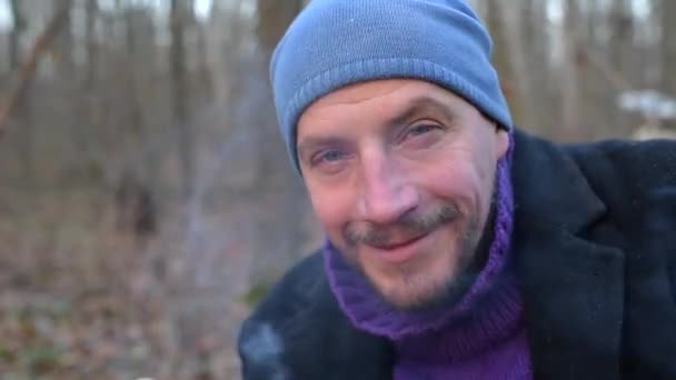Gros plan portrait d'un homme qui fume et boit du thé dans une tasse en métal dans la forêt, regarde dans la caméra et sourit . — Video