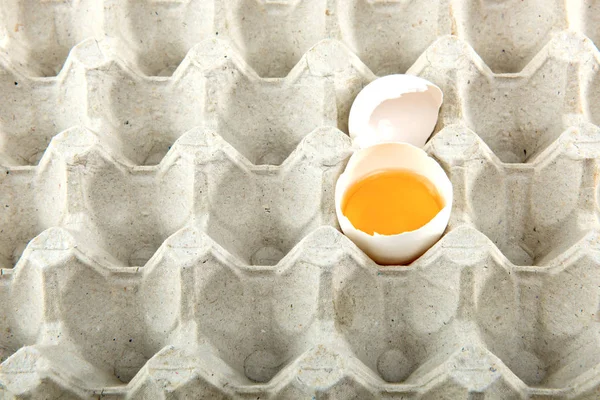 Chicken egg is half broken in egg tray. Close up.