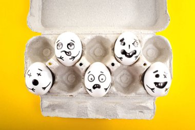 Paskalya yumurtaları ile çizilmiş Karikatür yüzler Sarı zemin üzerine karton bir tepsi içinde. Yakın çekim.