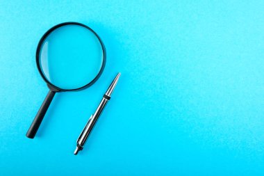 Büyüteç ve kalem mavi masada. Üstten Görünüm.