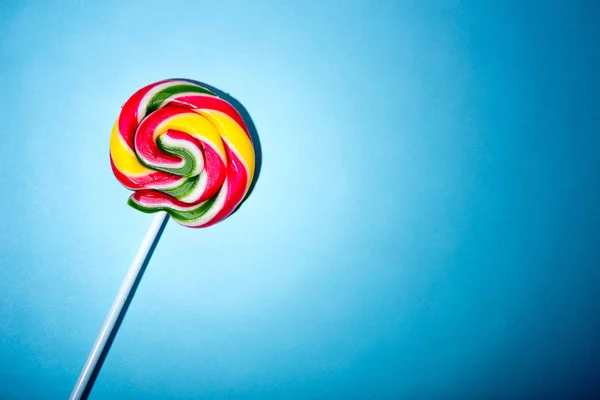 Colorful spiral lollipop candy on stick. On a blue background.