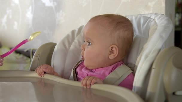 Klein schattig meisje zit achter een kinderstoel en speelt met lepel. Close-up. — Stockvideo