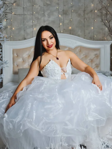 Young bride in a luxurious dress on a large bed.